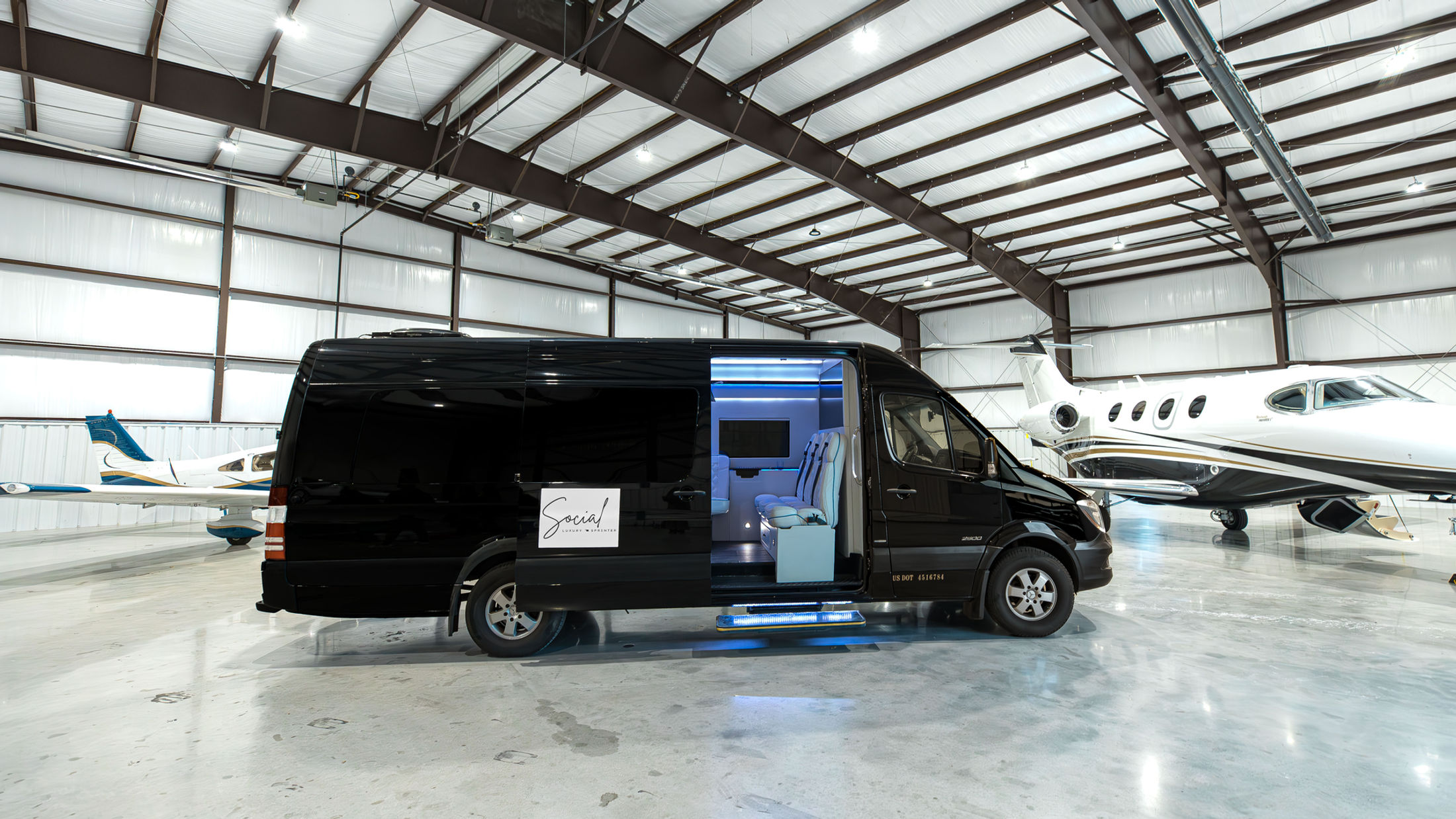 Black luxury Mercedes Sprinter van parked beside private jets in a Tulsa hangar
